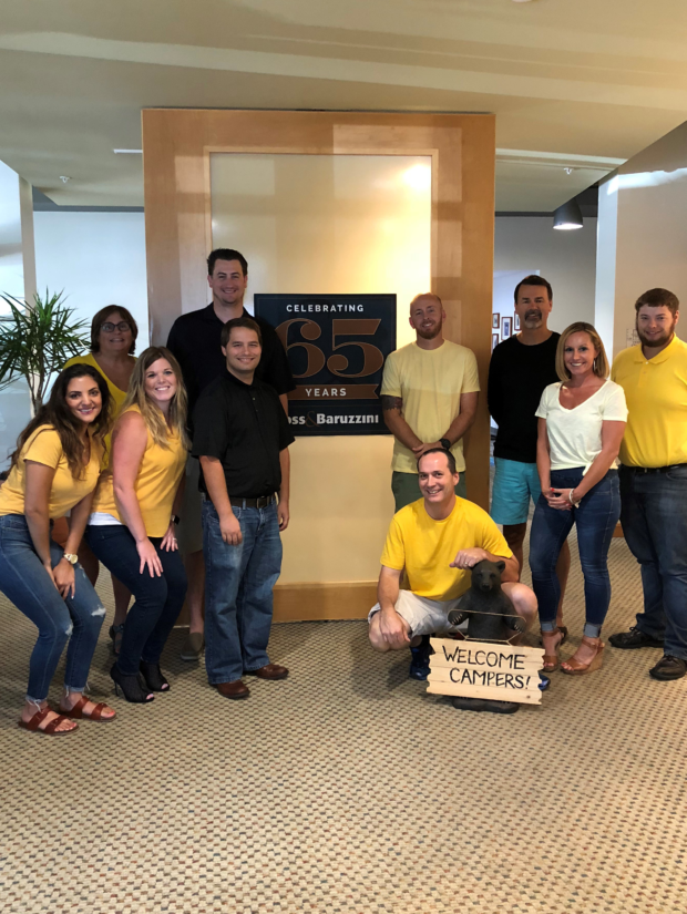 Small Group of Ross & Baruzzini employees standing by the company's 65th anniversary sign
